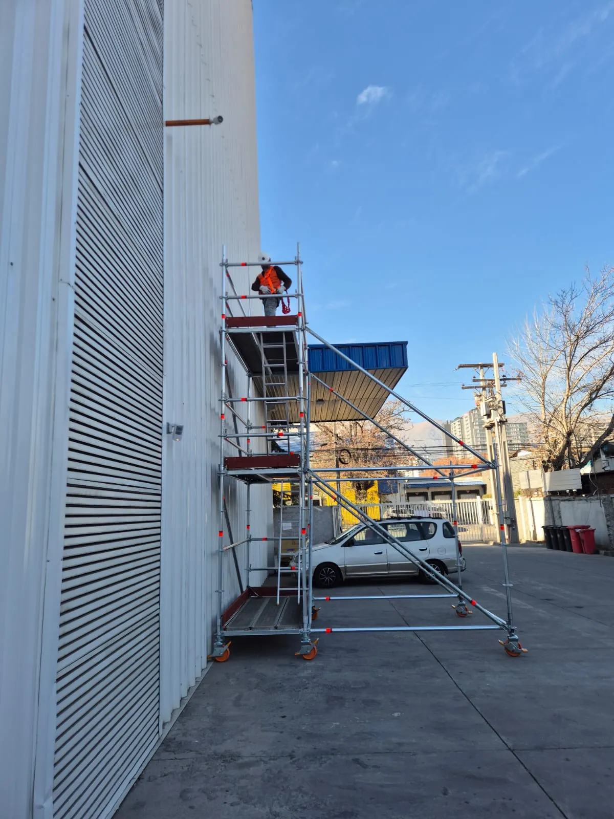 Operario con casco y chaleco de seguridad trabajando en la plataforma superior de andamio Layher