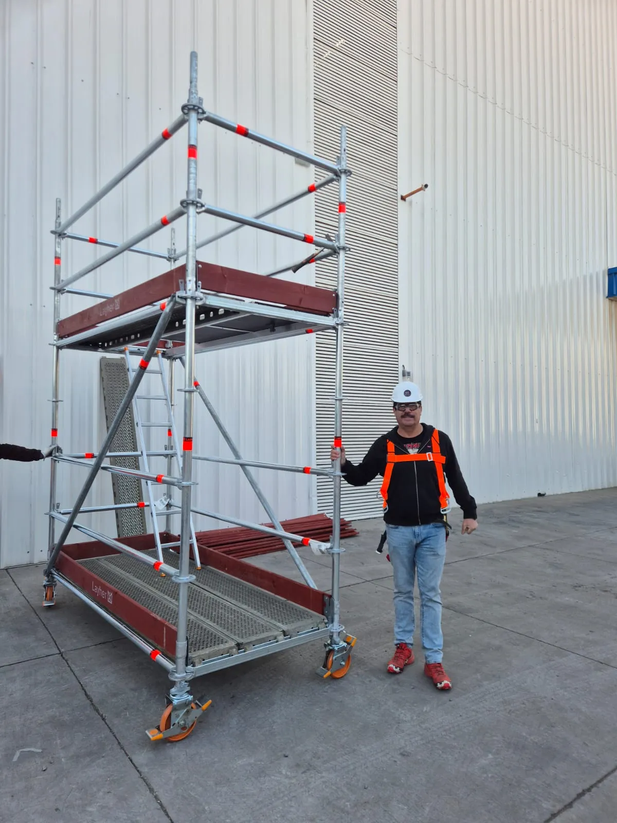 Operario de Modulares 360 con casco blanco, arnés de seguridad y torre Layher en terreno