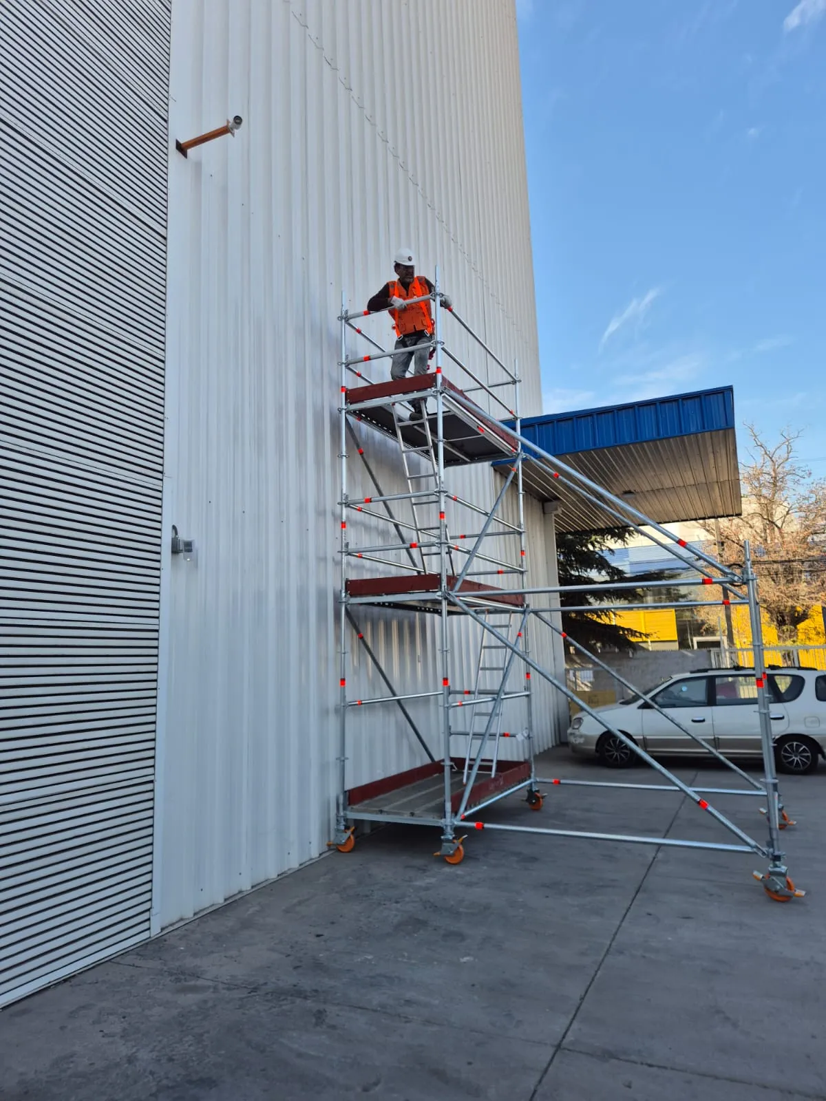 Torre de andamio Layher montada frente a muro industrial de chapa, con operario en plataforma superior